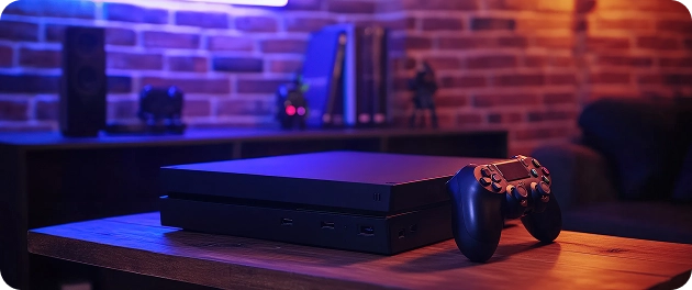 Een spelconsole en een controller op een houten tafel met neonverlichting en een bakstenen muur op de achtergrond